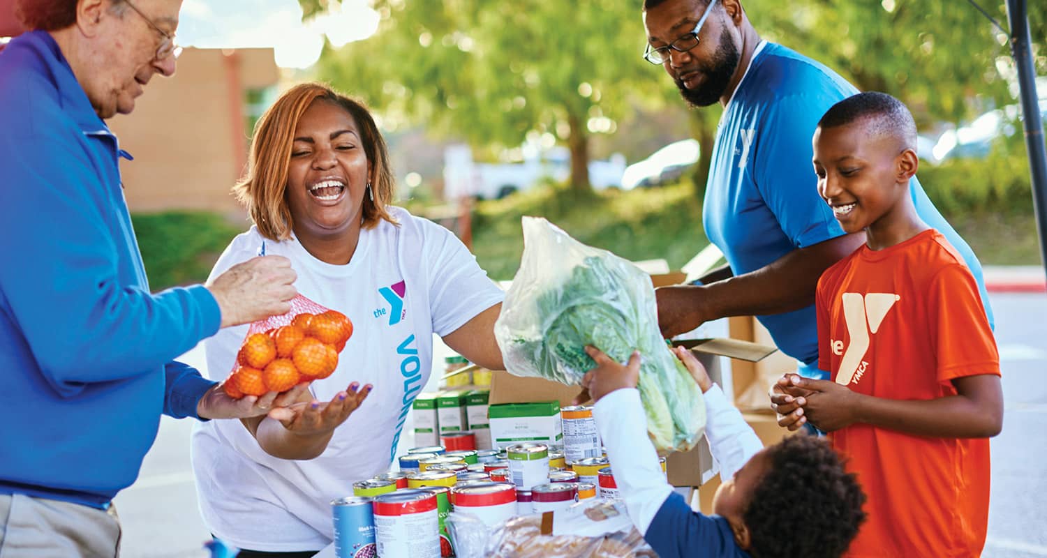 Volunteers and children at a community food drive, smiling while distributing fresh produce and canned goods outdoors.