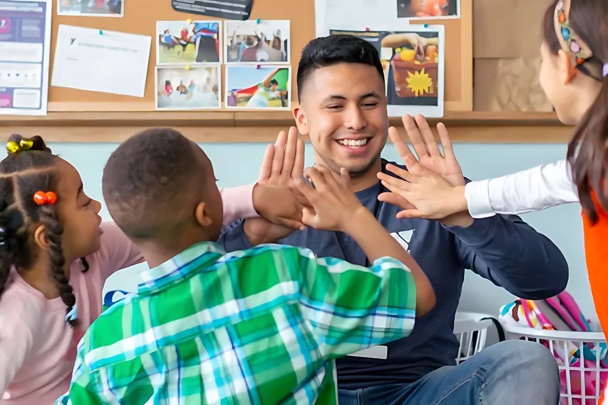 A smiling instructor engages with children, giving high-fives during an activity in a colorful classroom setting.