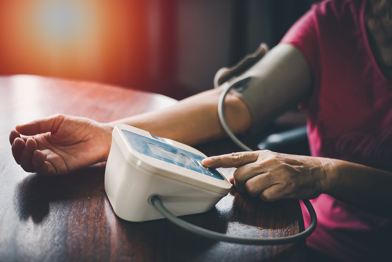 Close-up of a person checking their blood pressure with a digital monitor at a wooden table.