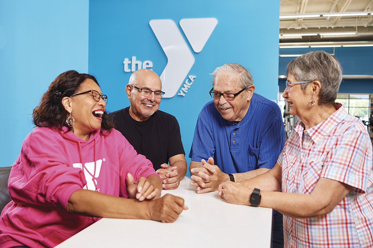 A group of senior adults gather at the front desk of the local YMCA and talk with one another.