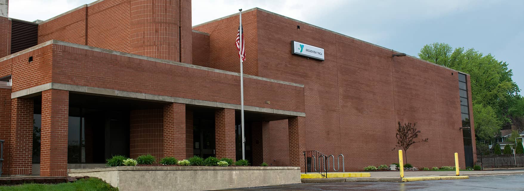 Exterior view of a red-brick YMCA building with an American flag and green landscaping in the foreground.