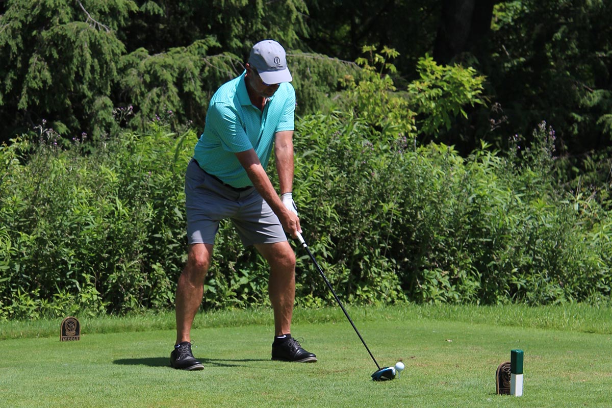 Man preparing to tee off on a lush green golf course surrounded by trees and shrubs.