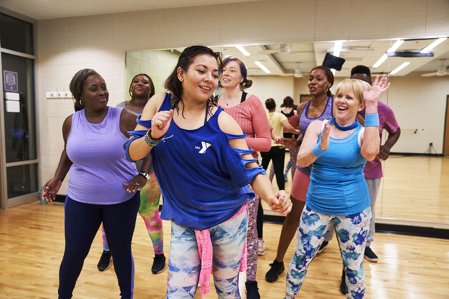 Diverse group of people smiling and dancing during a fitness class in a mirrored studio at the YMCA.