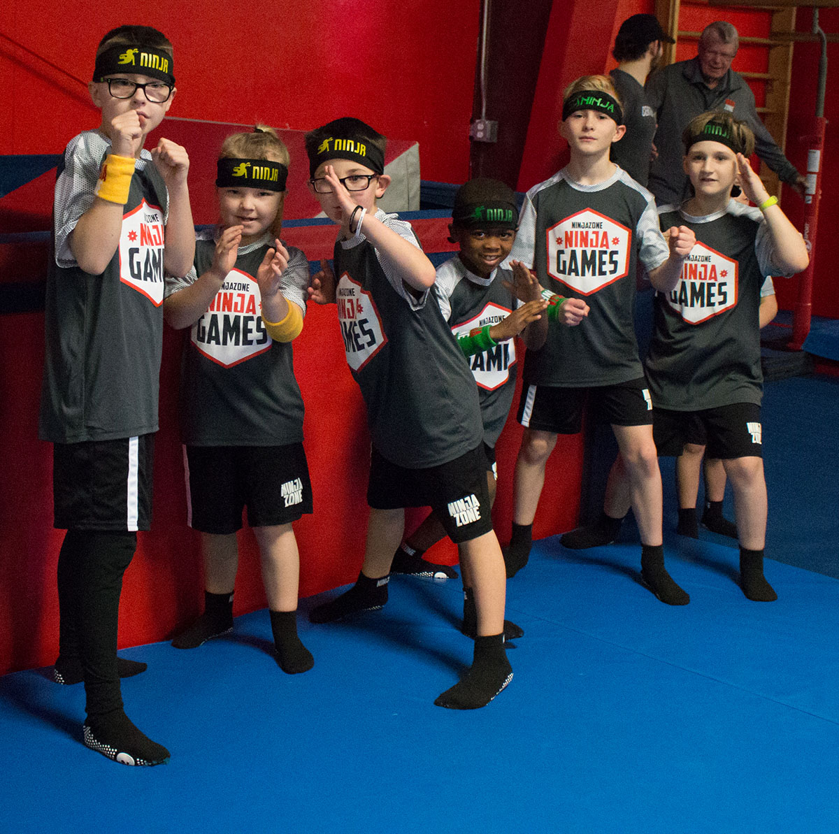 Group of children wearing Ninja Games shirts and headbands posing in a gym environment, participating in a ninja-themed event or activity.