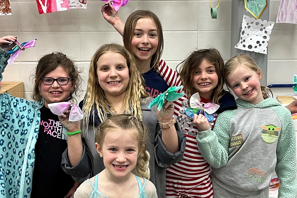 Group of smiling children showing off colorful handmade crafts in a classroom setting.