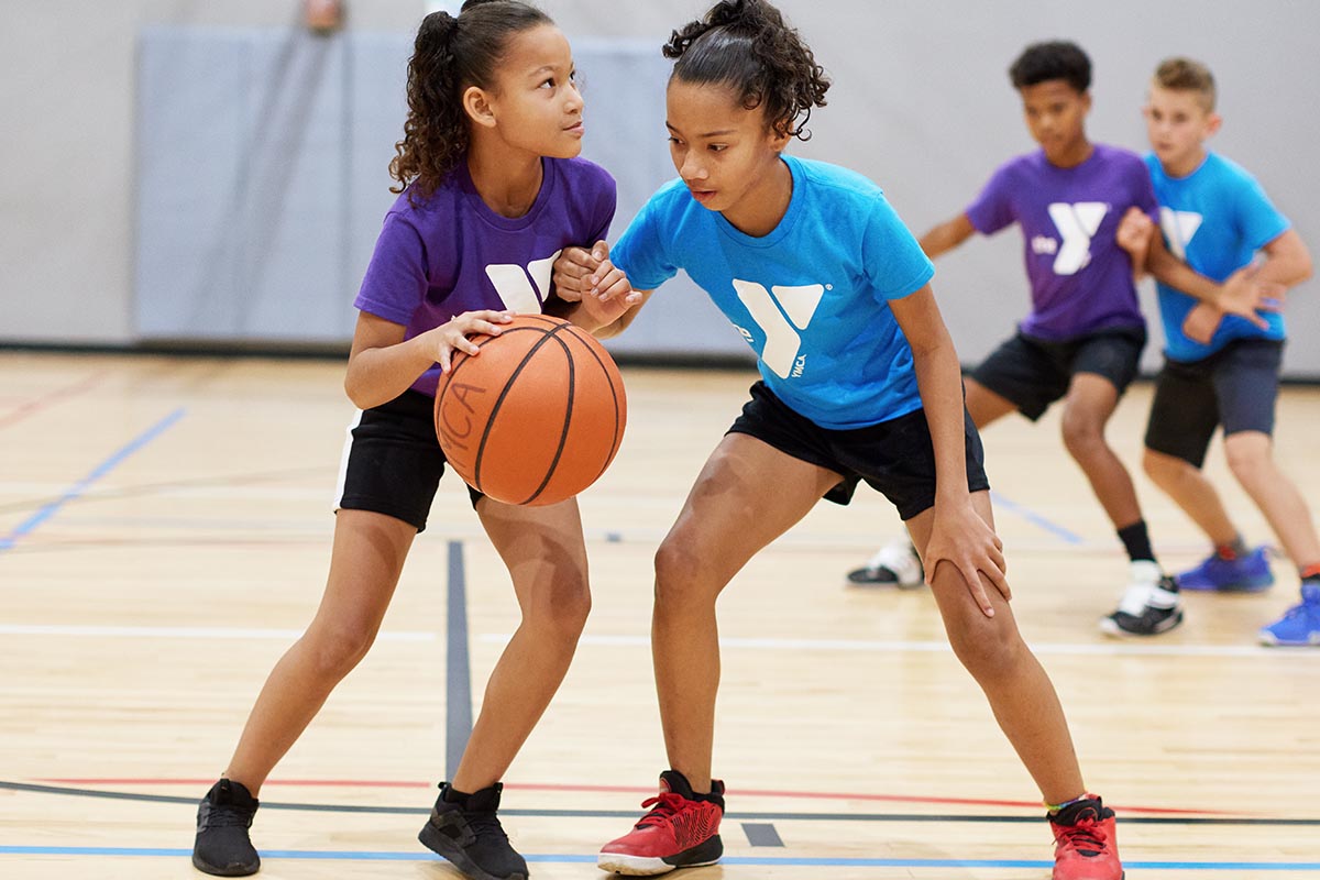 Children practicing basketball skills during a youth sports class in a gymnasium.