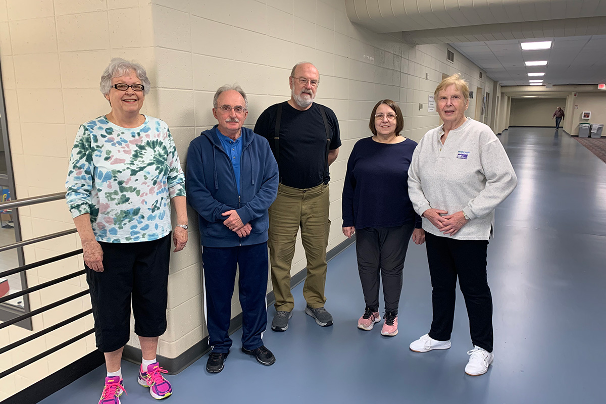 A group of older adults standing in an indoor walking track area, smiling after a fitness activity.