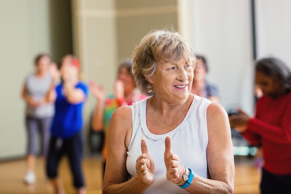 Smiling senior woman clapping during a group fitness class in a community center.