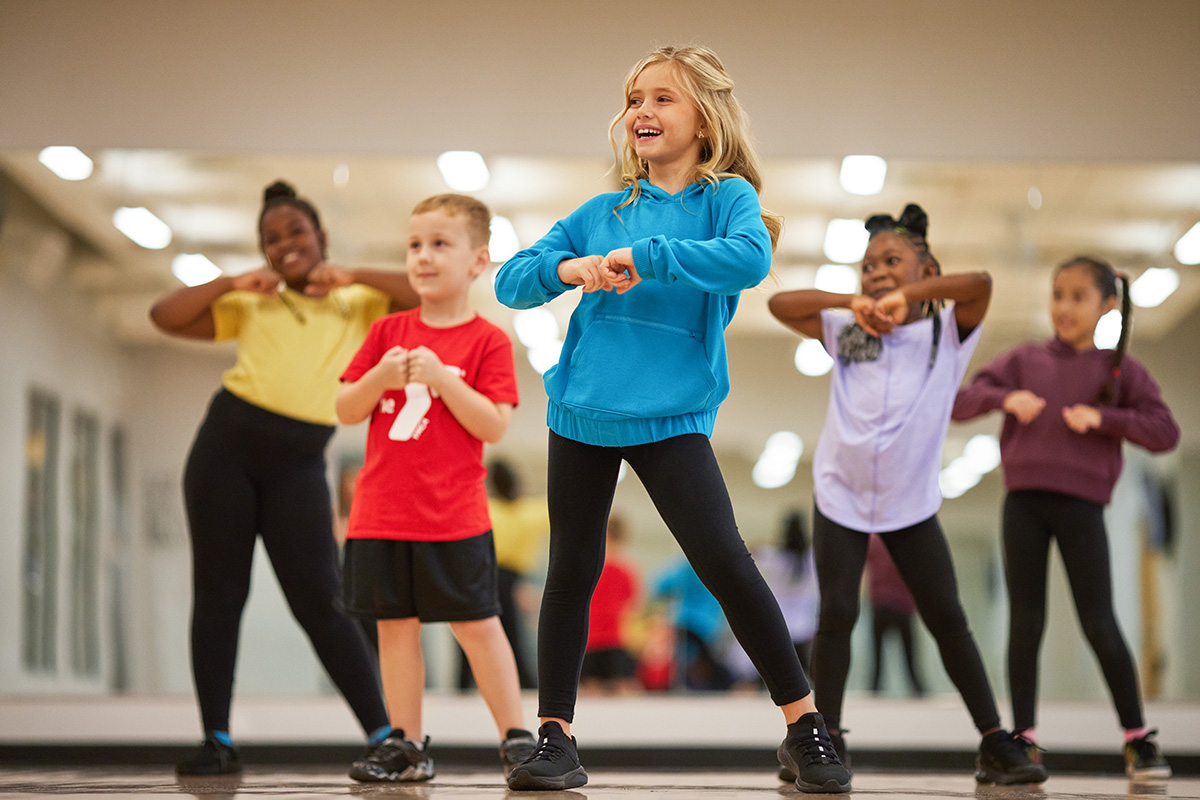 Children participating in a lively dance class, smiling and following movements in a mirrored studio.