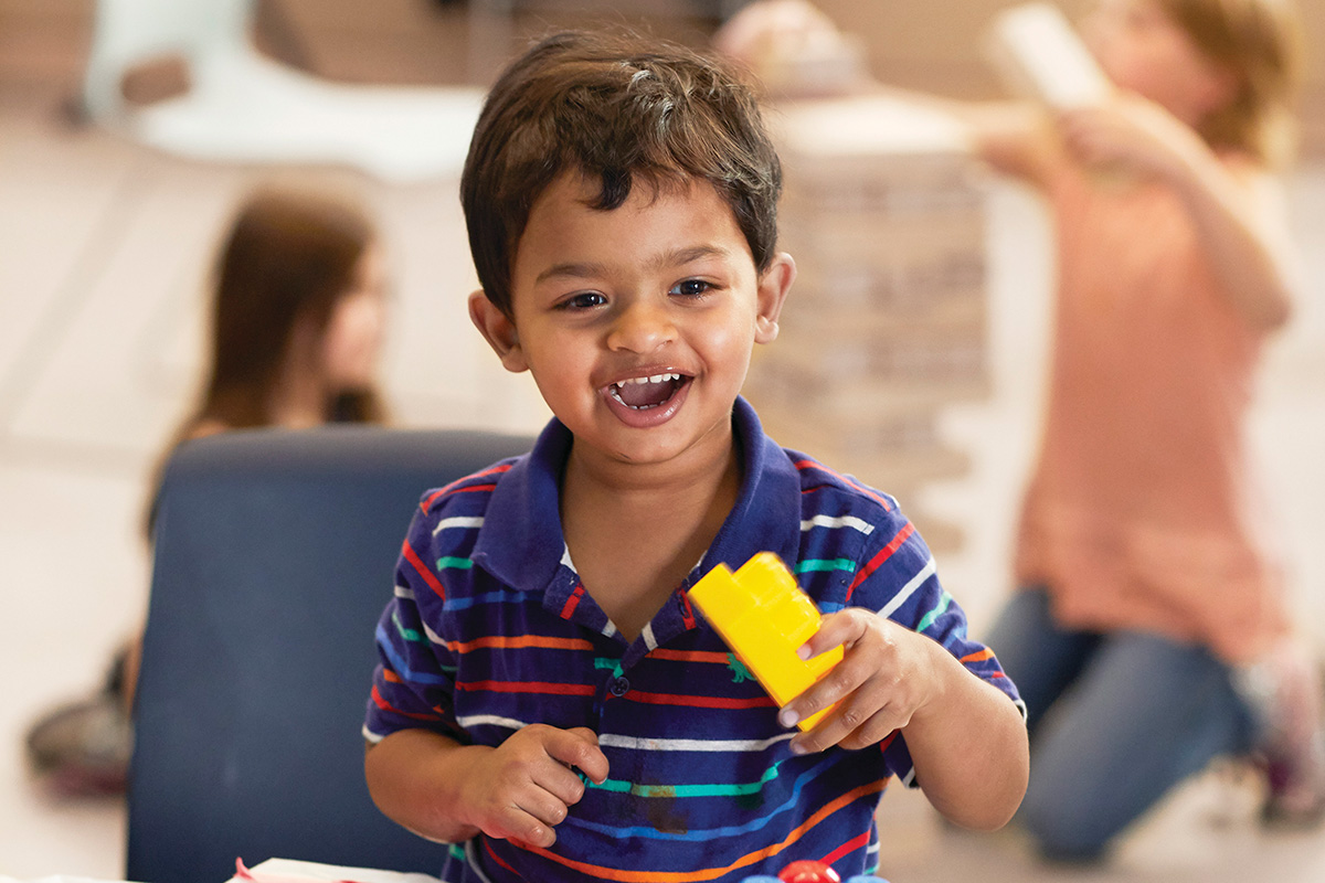 Young child smiling while playing with colorful building blocks in a classroom setting.