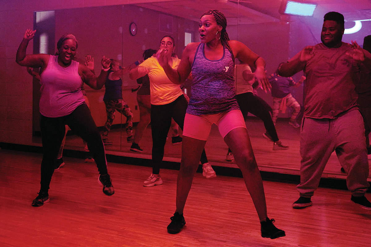 A group of adults participates in an energetic dance fitness class under colorful lighting in a mirrored studio.