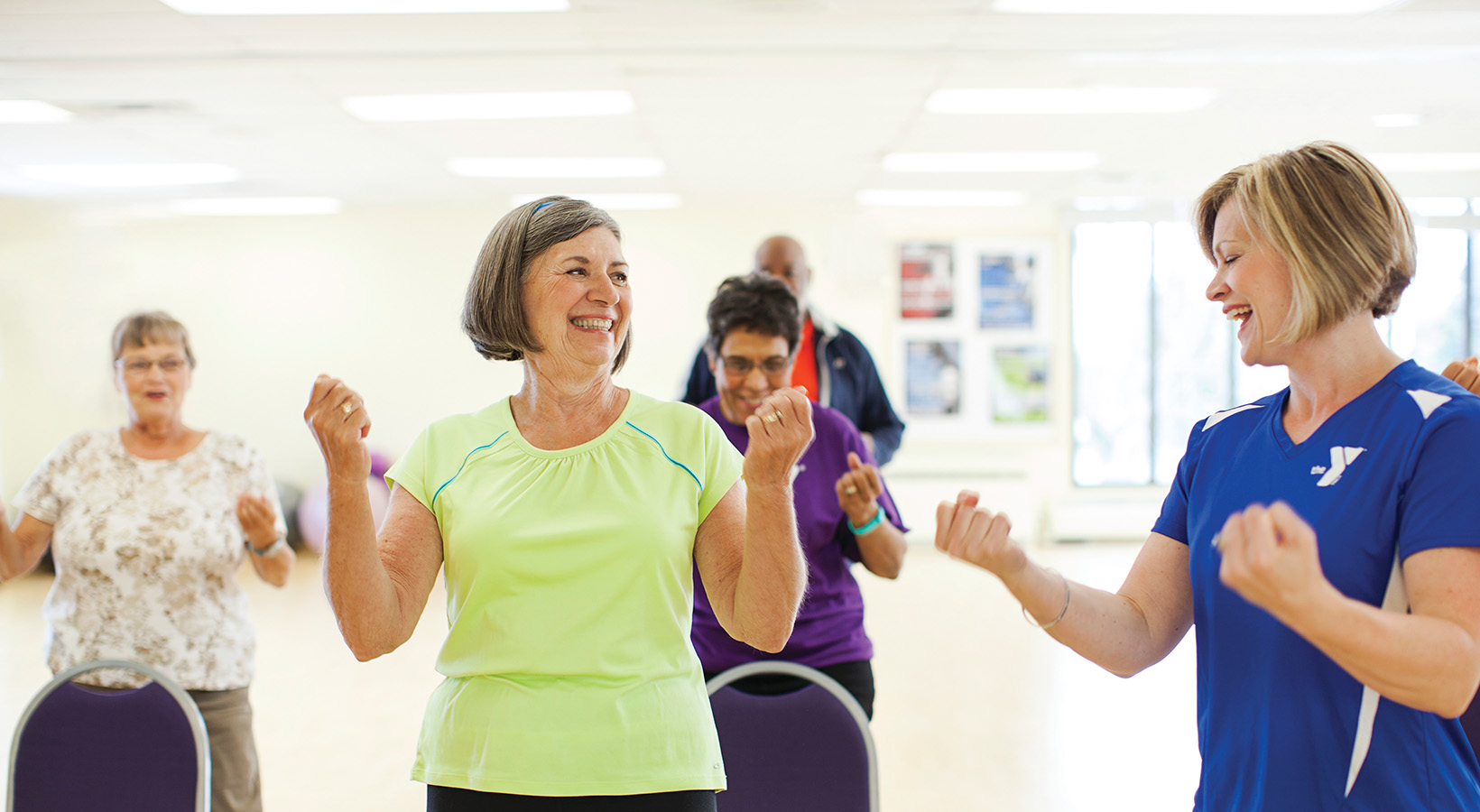 A group of older adults participates in a lively fitness class, led by an enthusiastic instructor in a bright studio.