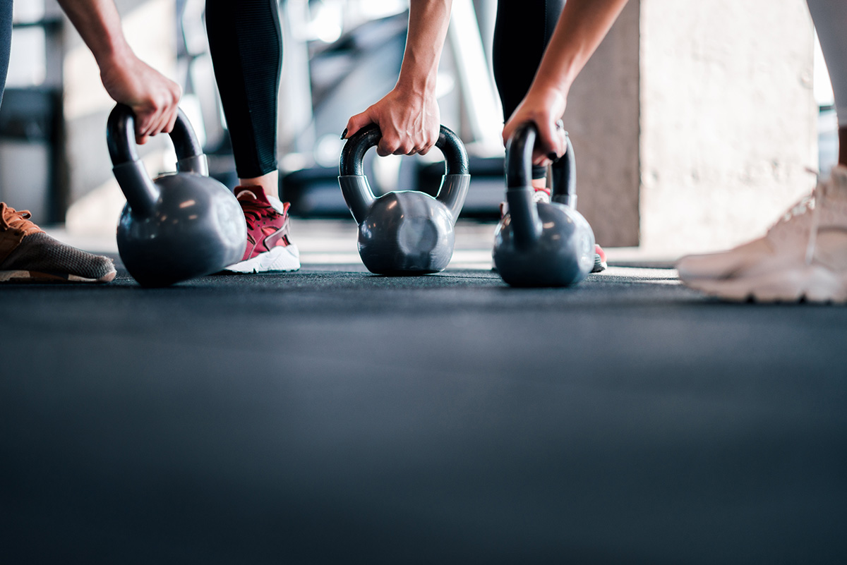 Close-up of people gripping kettlebells during a workout on a gym floor.