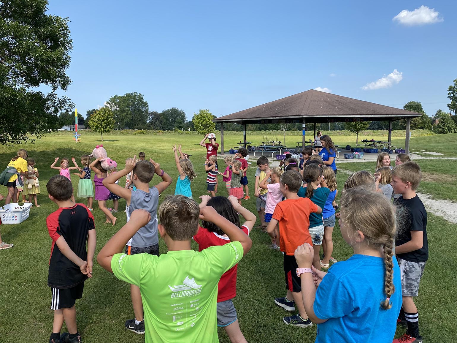 Children participating in an outdoor activity near a pavilion on a sunny day.