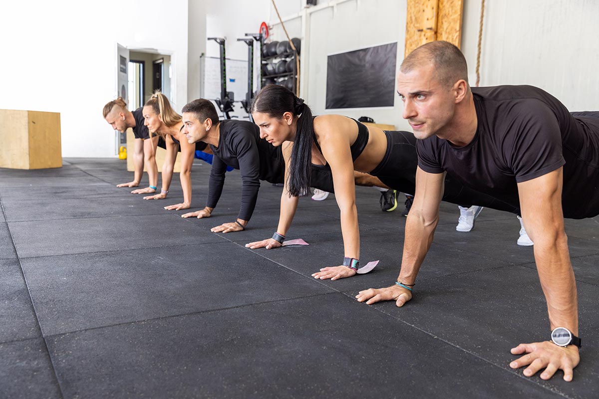 A group of adults holds a plank position during a fitness class in a gym.