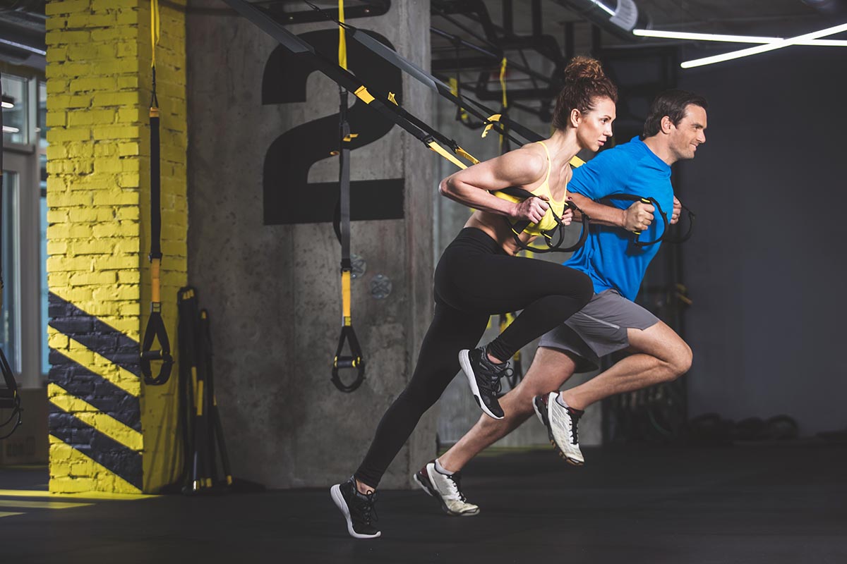 A man and woman perform resistance training with suspension straps in a modern gym.