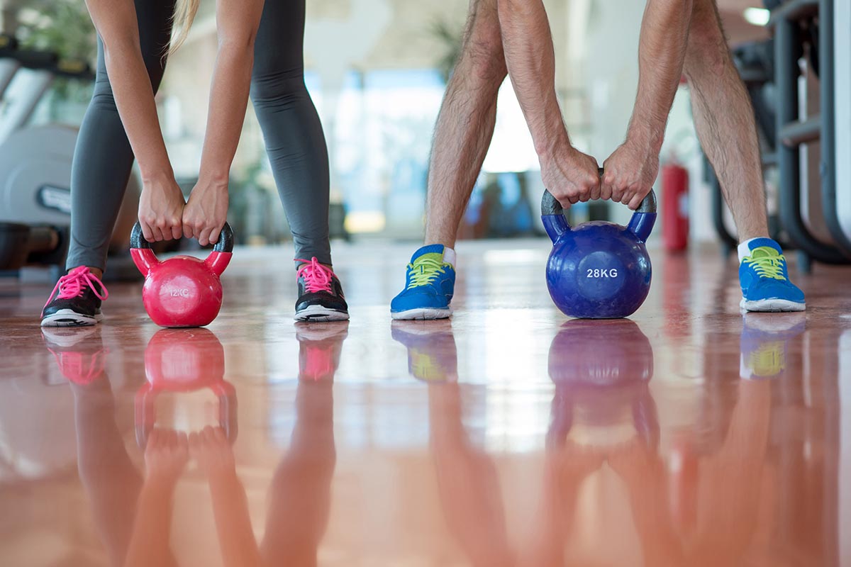 Two people grip kettlebells, one red and one blue, during a workout on a gym floor.