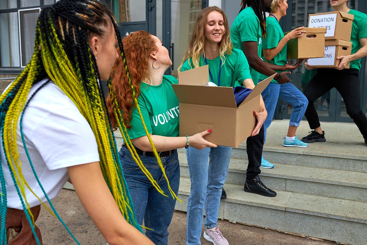 Group of volunteers in green shirts working together to carry donation boxes filled with clothes and supplies outside a building.