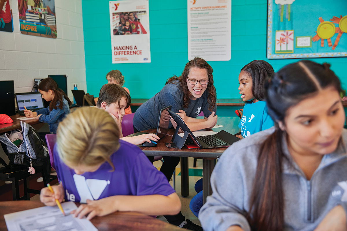 A group of students and a teacher study on a computer in a classrom setting.